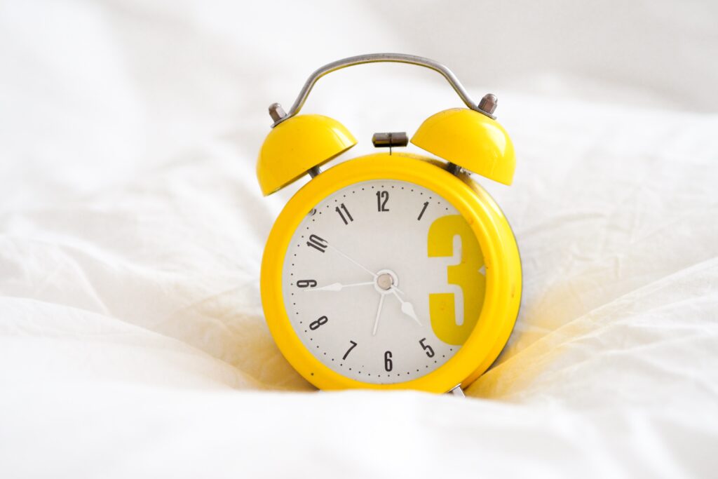 a photo of a yellow alarm clock on a bed, used in the blog on building a successful morning routine
